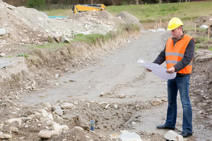 Phase 2 Environmental Site Assessments in New York , A Site Inspector in a safety vest examines plans on a dirt site surrounded by rocks and machinery